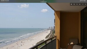 Un balcón con vista a una playa, un muelle y un paisaje urbano distante.