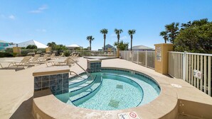 Zona de piscina con sillas de descanso, un jacuzzi y un deck de piscina cercado.