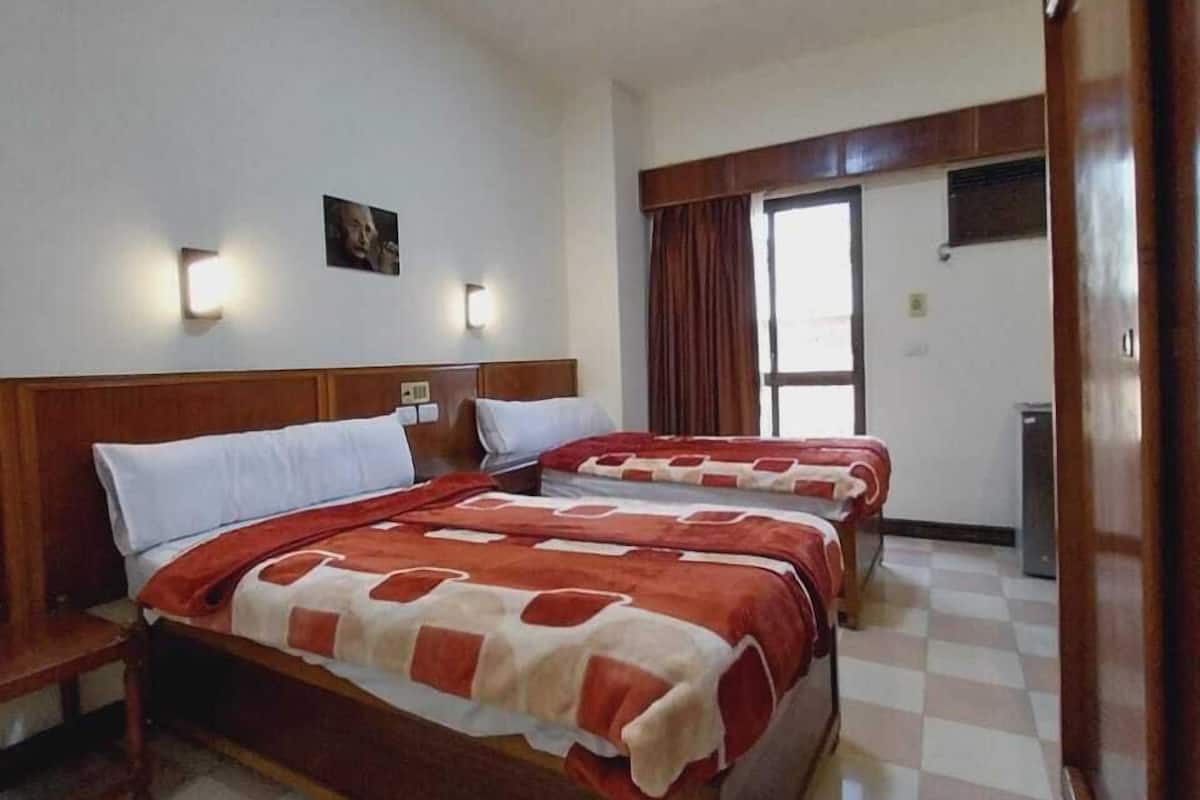 Quarto de hotel com duas camas, cabeceira de madeira, piso xadrez e luminária no teto.
