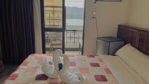Een hotelkamer met een bed, nachtkastje, stoel en uitzicht op een balkon met een hekwerk.