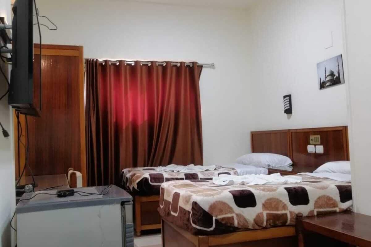 Quarto de hotel com duas camas, uma escrivaninha, televisão e uma janela com cortinas.