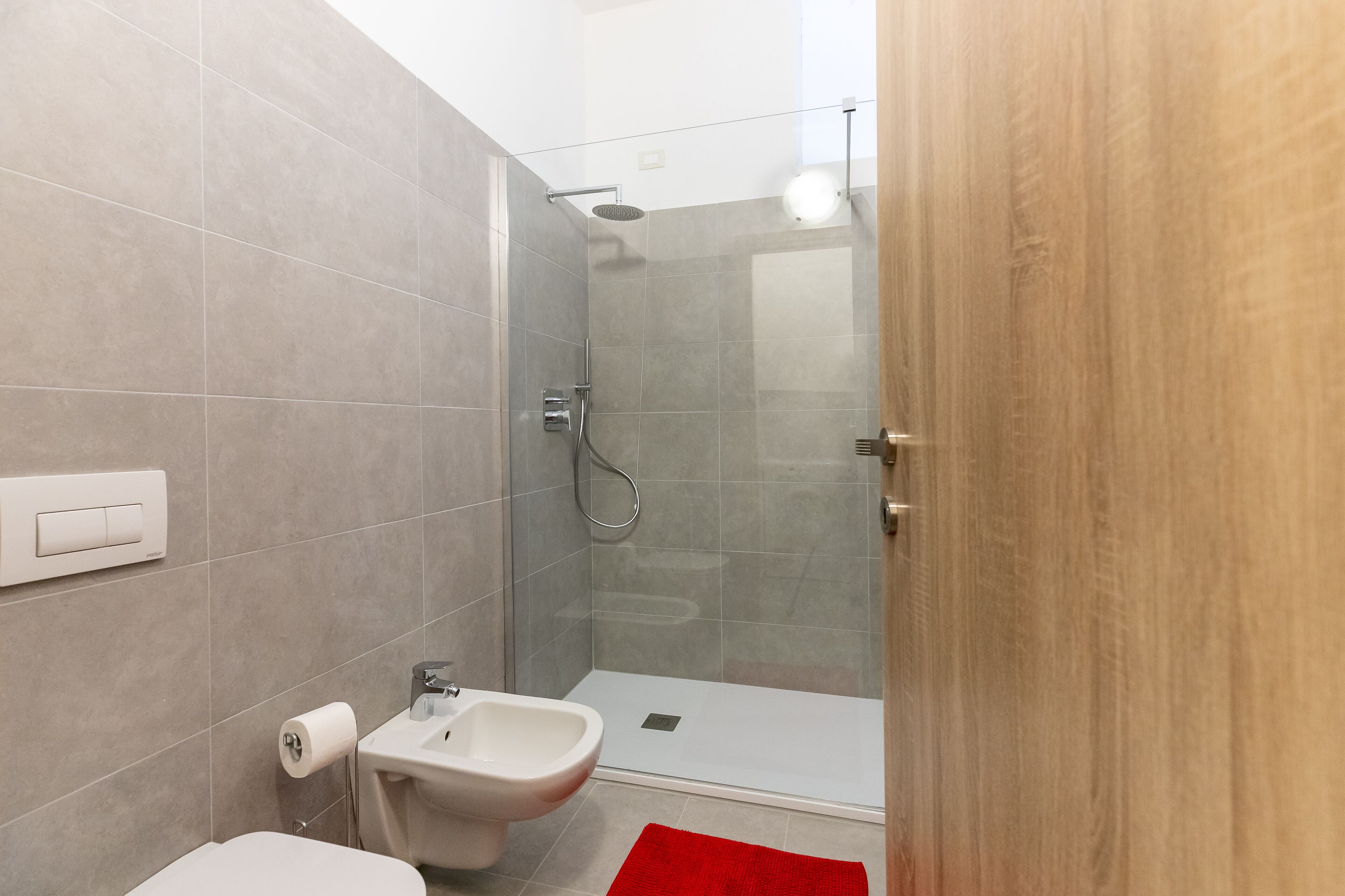 Uma casa de banho moderna com chuveiro, sanita, bidé e um tapete vermelho.