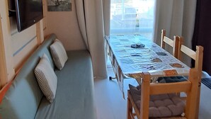 A compact room with a sofa, a dining table, and a television mounted on the wall. - Mobil Home à 1.5km du Centre Ville, en en Plein Cœur de la Montagne Corse (Corte)