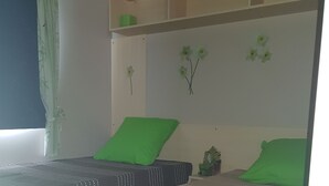A bedroom with two beds, each with a green pillow and a patterned bedspread. There is a small shelf with a green box and a potted plant. - Mobil Home à 1.5km du Centre Ville, en en Plein Cœur de la Montagne Corse (Corte)