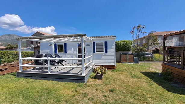 A mobile home with a patio area, a small garden, and a neighboring house. - Mobil Home à 1.5km du Centre Ville, en en Plein Cœur de la Montagne Corse (Corte)