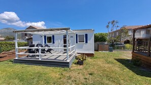 Une maison mobile dotée d’un patio, d’un petit jardin et située à proximité d’une autre maison.