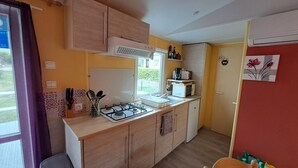 A compact kitchen with a gas stove, microwave, and a small refrigerator. There is a window providing natural light and a view of the outside. - Mobil Home à 1.5km du Centre Ville, en en Plein Cœur de la Montagne Corse (Corte)