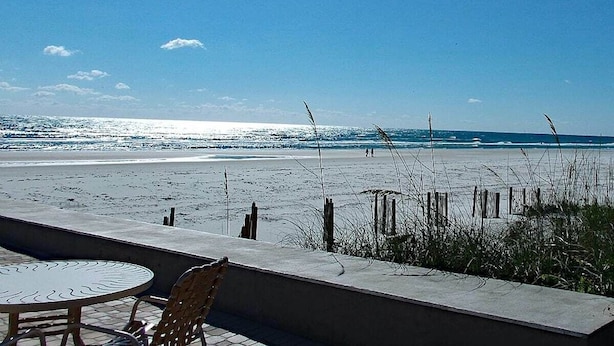 Vista de la playa con una mesa y sillas, una barrera de hormigón y una valla de madera.