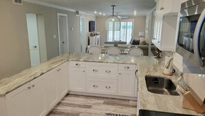 Cocina con armarios blancos, encimera de mármol y pileta de acero inoxidable.