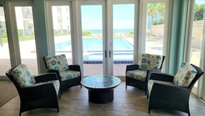 Una habitación con cuatro sillas de mimbre con cojines florales, una mesa redonda de centro y puertas de cristal que dan a una zona de piscina.
