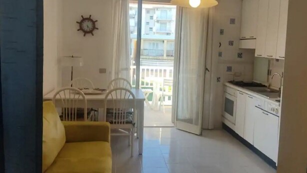 Un espace de vie compact comprenant un coin repas, un canapé, une cuisine et une porte-fenêtre coulissante donnant sur un balcon extérieur.