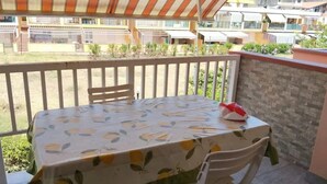 Un balcon avec une table recouverte d’une nappe à motifs floraux, une chaise et un sac rouge posé sur la table.