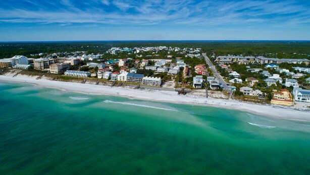 Une vue aérienne d’une ville côtière avec une plage, des maisons et un ciel dégagé.