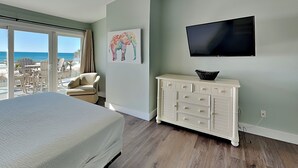 A bedroom with a bed, a ceiling fan, a television, a dresser, and a window overlooking the beach. - Charline Beachside Villa | Gulf Front Luxury (Panama City Beach)