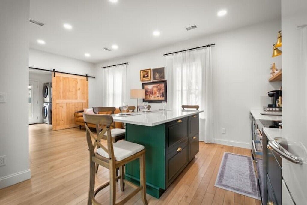 A modern kitchen with a central island, wooden chairs, and a view into the dining area.