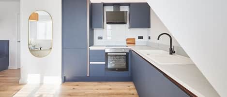 A modern kitchen with built-in appliances, a large window, and a wooden floor.