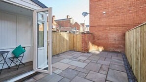 A patio with stone flooring, a wooden fence, and a white door leading to a room with a teal cushion and a small table. - Host & Stay | Station View (Saltburn-by-the-Sea)
