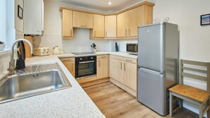 A compact kitchen with wooden cabinets, a stainless steel refrigerator, a microwave, an oven, and a sink. - Host & Stay | Station View (Saltburn-by-the-Sea)