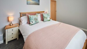 A neatly made bed with a pink blanket and floral pillows, a bedside lamp, and a painting on the wall. - Host & Stay | Station View (Saltburn-by-the-Sea)