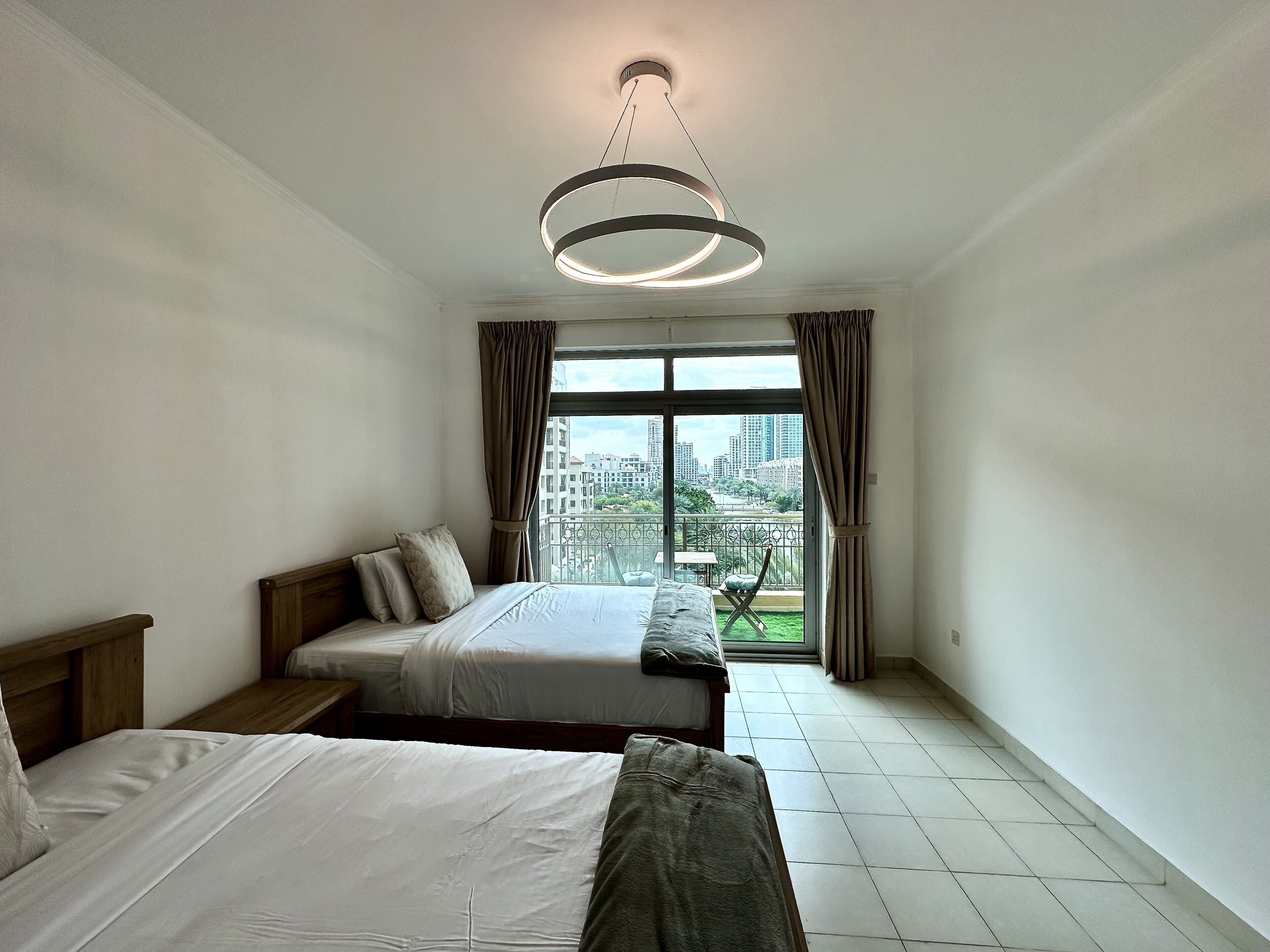 A hotel room with two beds, a view of the cityscape through large windows, and a modern pendant light.
