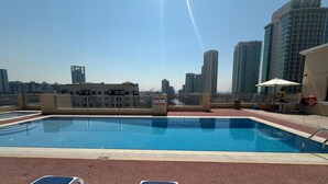 Una piscina sul tetto con poltrone relax e vista sullo skyline della città, sotto un cielo sereno.