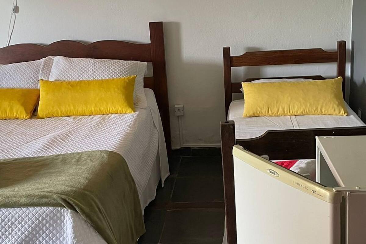 A room with two beds, each with white bedding and yellow pillows, a wooden headboard, and a wall-mounted light fixture with a floral design.
