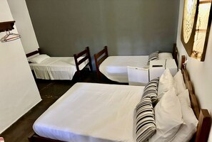 Quarto pequeno e compacto com duas camas individuais, cabeceiras de madeira e uma mesinha.