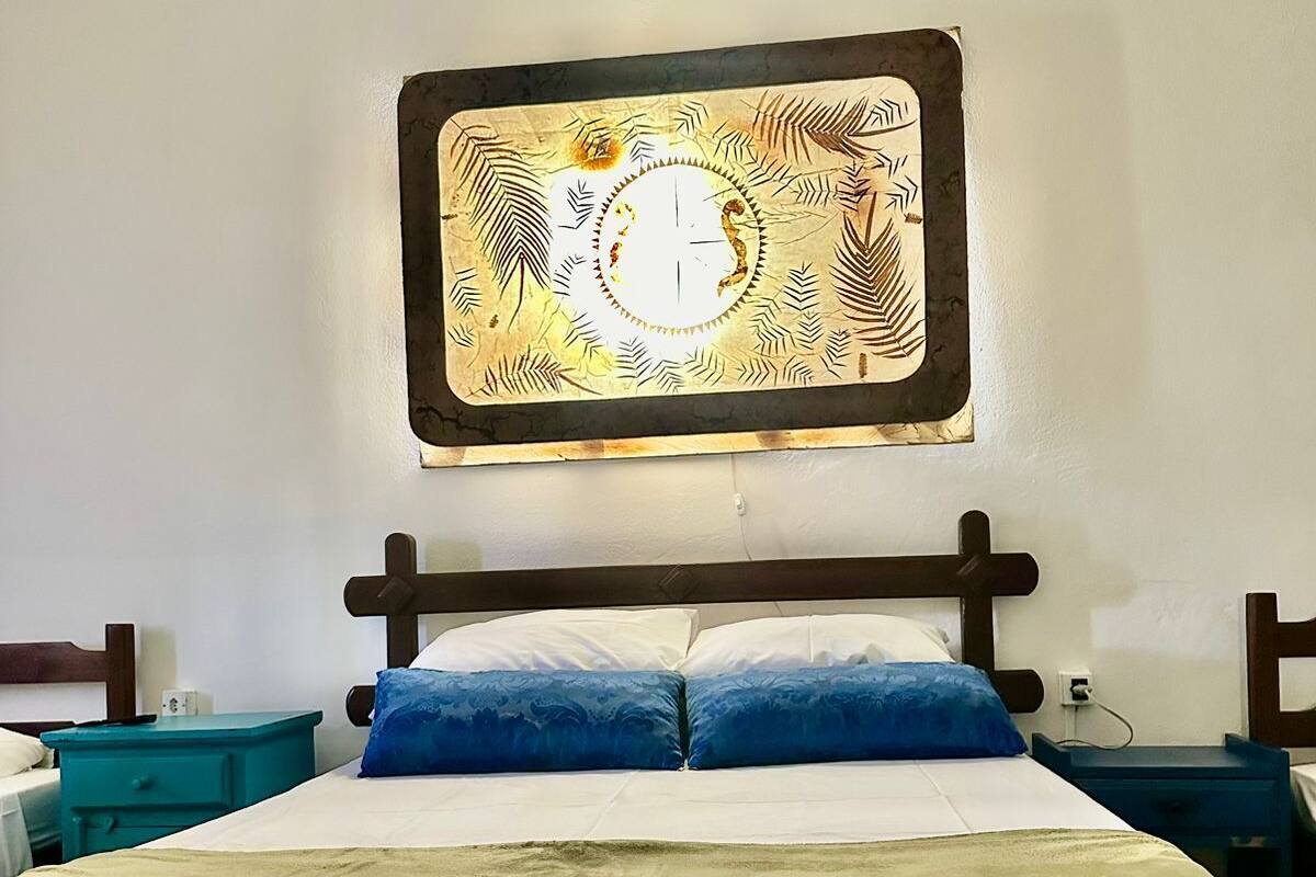 A neatly made bed with a green blanket, two blue pillows, and a wooden headboard. There is a wall-mounted artwork above the bed.