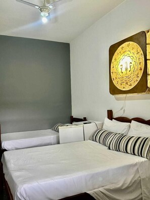 A hotel room with a large bed, two smaller beds, a ceiling fan, and a decorative wall light.