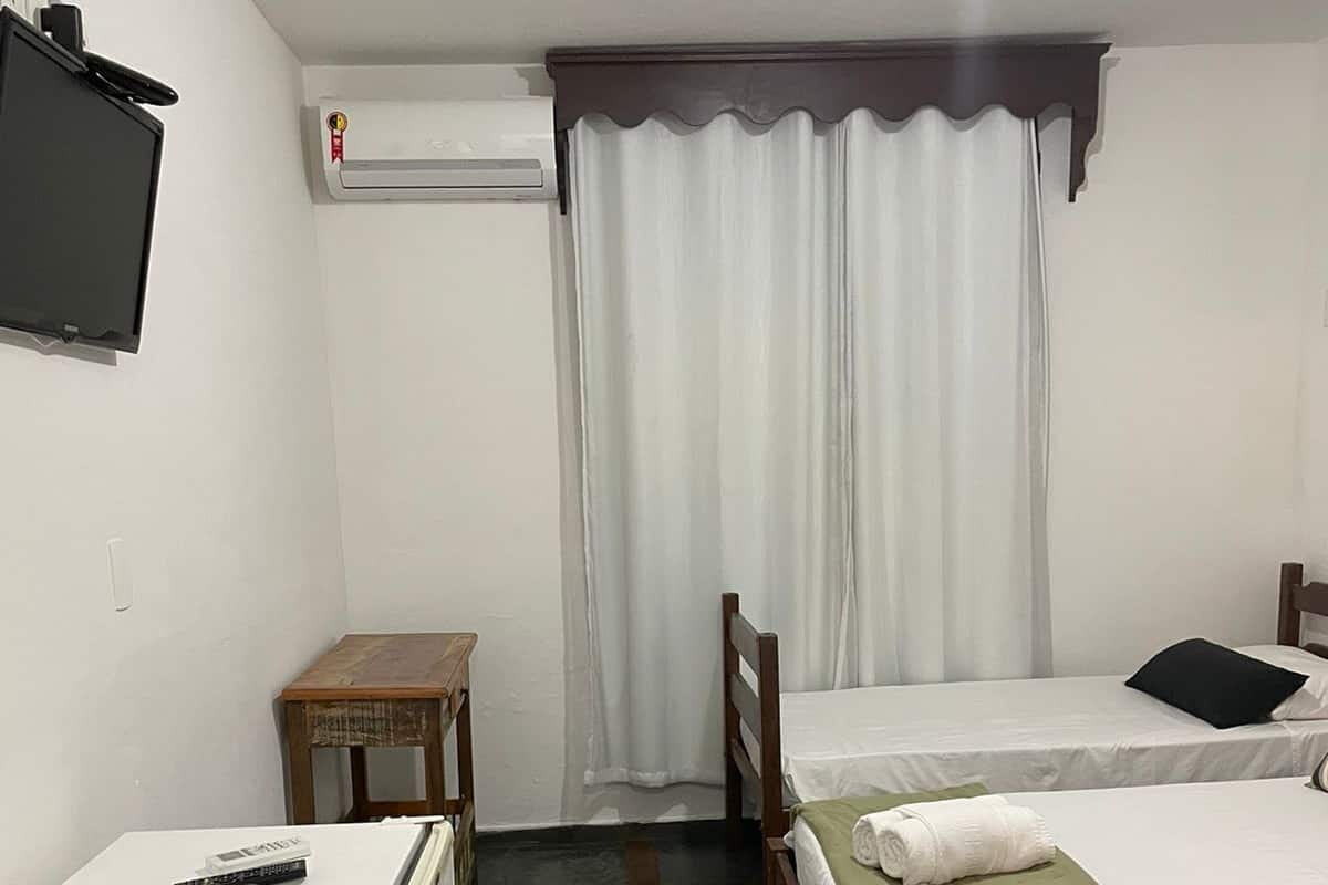 A small, compact room with a single bed, a small table, a refrigerator, and a television mounted on the wall.