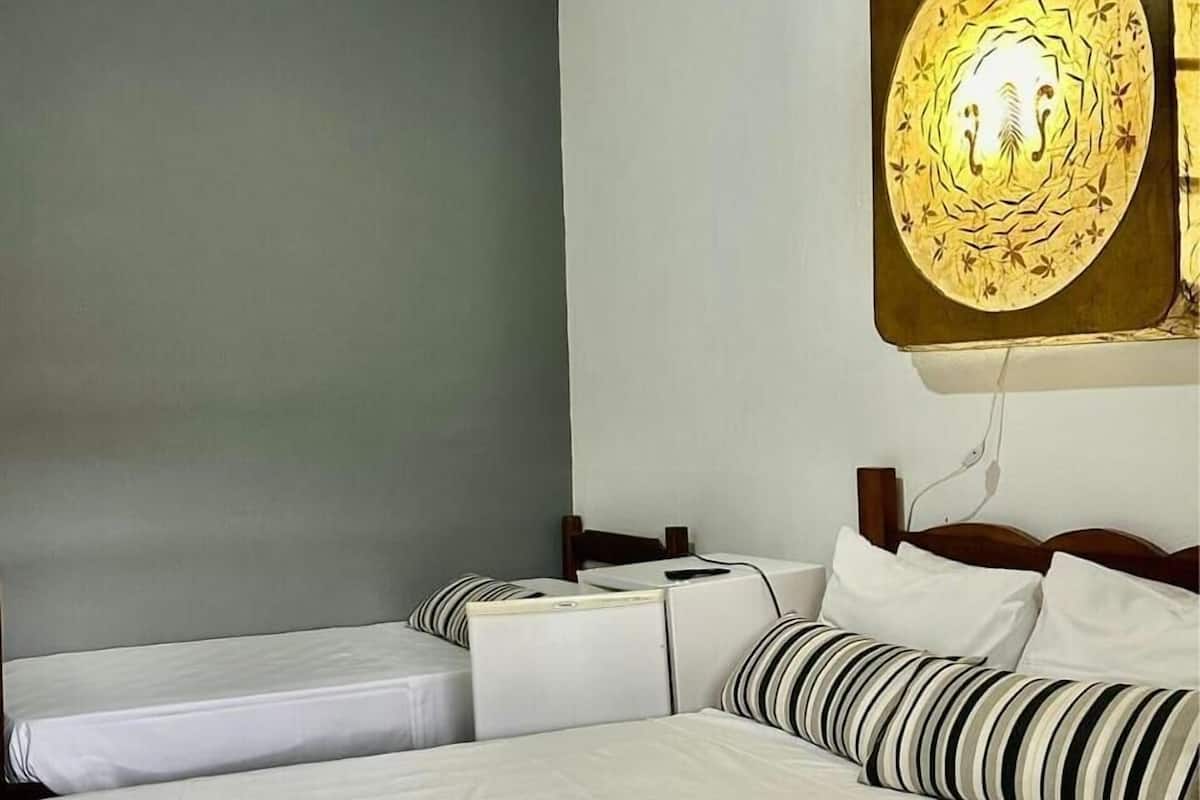 A hotel room with two single beds, a large wall-mounted artwork, and a ceiling fan.
