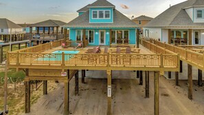 A wooden deck with a pool, a covered seating area, and a view of the beach.