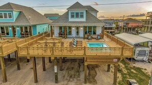 A waterfront property with a pool, deck chairs, and a covered area.