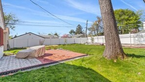A backyard with a covered patio area, a tree, and a well-maintained lawn.