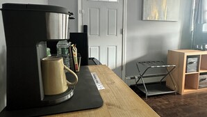 A kitchen with a coffee maker, a kettle, and a mug on a wooden countertop. There is a door with a window in the background.