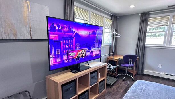 A modern hotel room with a large flat-screen TV, wooden furniture, a bed, and a desk with a chair.