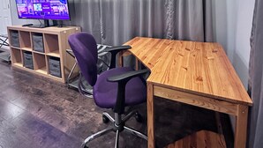 A room with a wooden desk, a purple office chair, a television on a stand, and a window with curtains.
