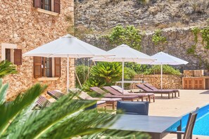 A poolside area with lounge chairs and umbrellas, a stone building, and a view of a rocky hillside. - Carritxo Finca for 8,  private pool, panoramic views, relax and tranquillity. (es carritxo)