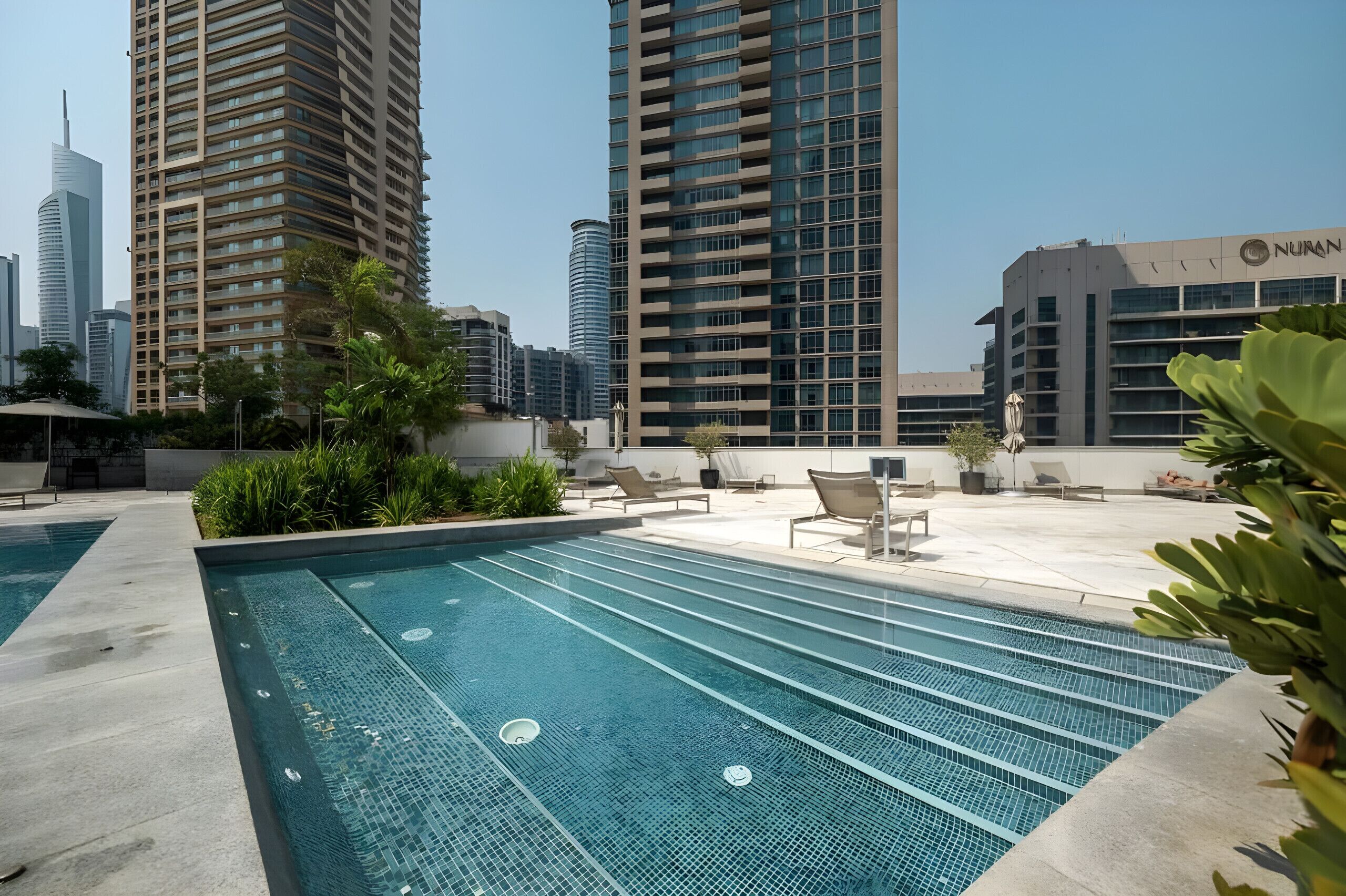 Une piscine avec des chaises longues et une vue sur de hauts immeubles.