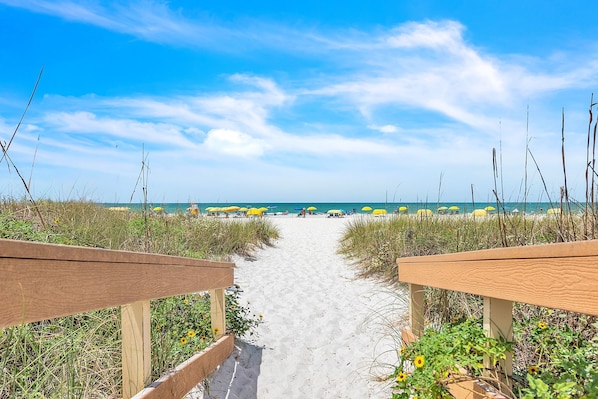 A beach path leading to the ocean with beach umbrellas and a wooden fence.