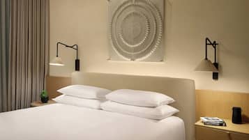 A neatly made bed with white linens, a small bedside table with a book and a black object, and two wall-mounted lamps.