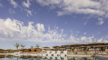 A resort pool area with lounge chairs and umbrellas, surrounded by buildings and palm trees.