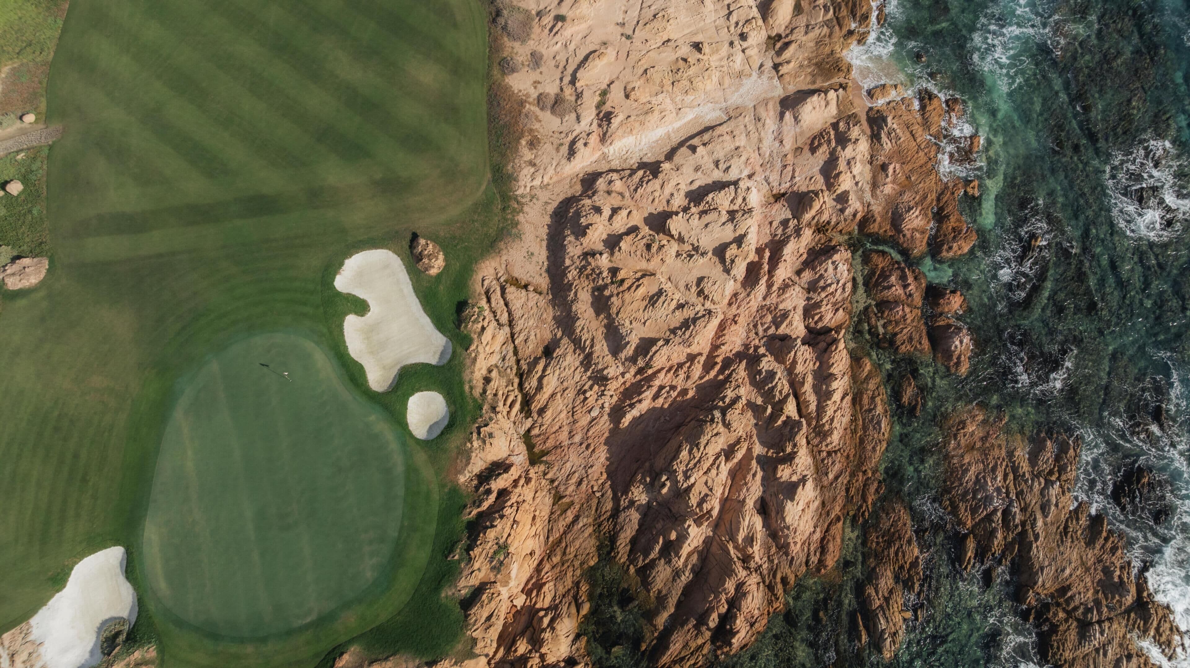 Vista aérea de un paisaje costero con un campo de golf, acantilados rocosos y aguas cristalinas.