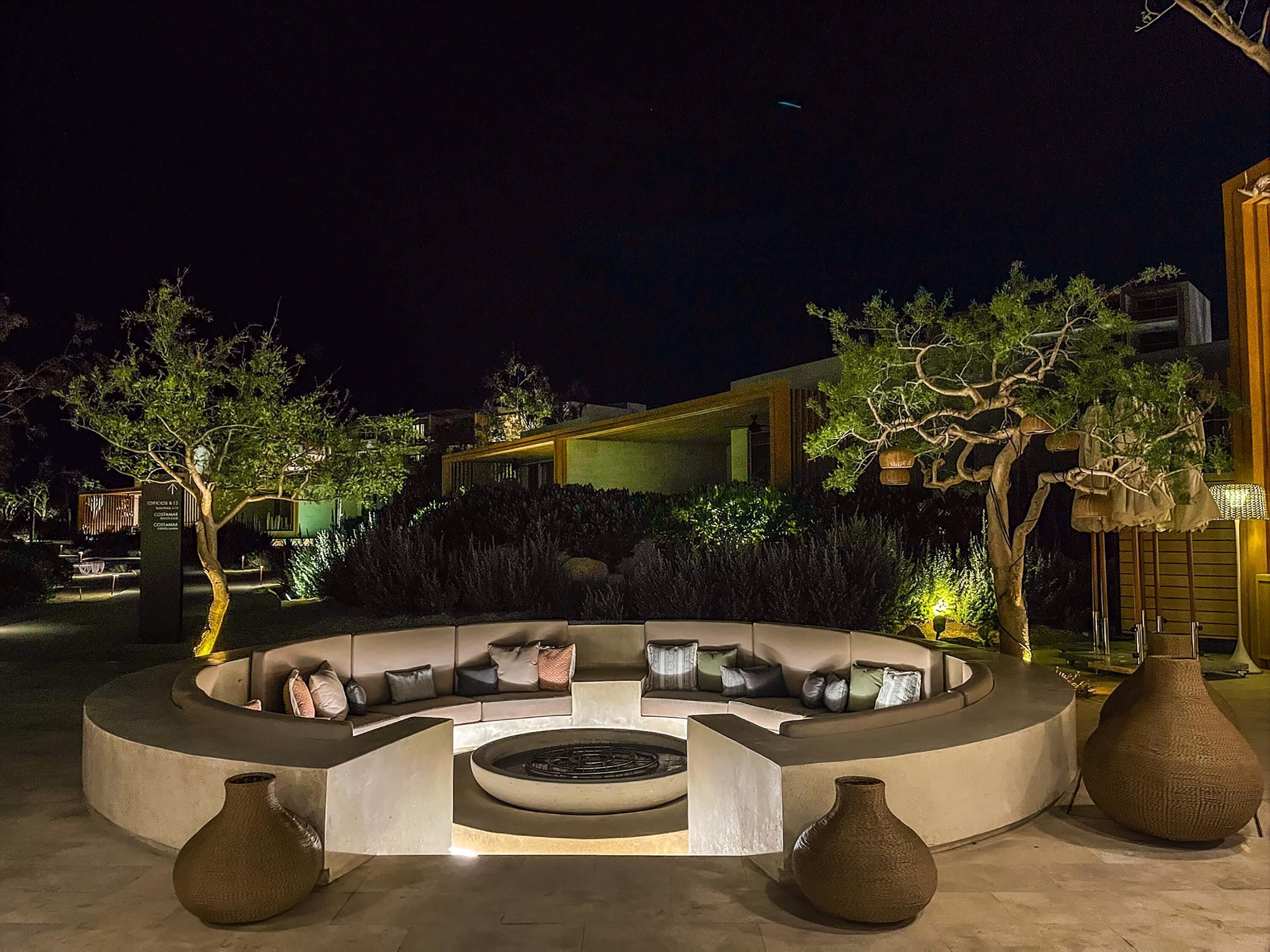 An outdoor seating area with a circular arrangement of sofas and a central fire feature.