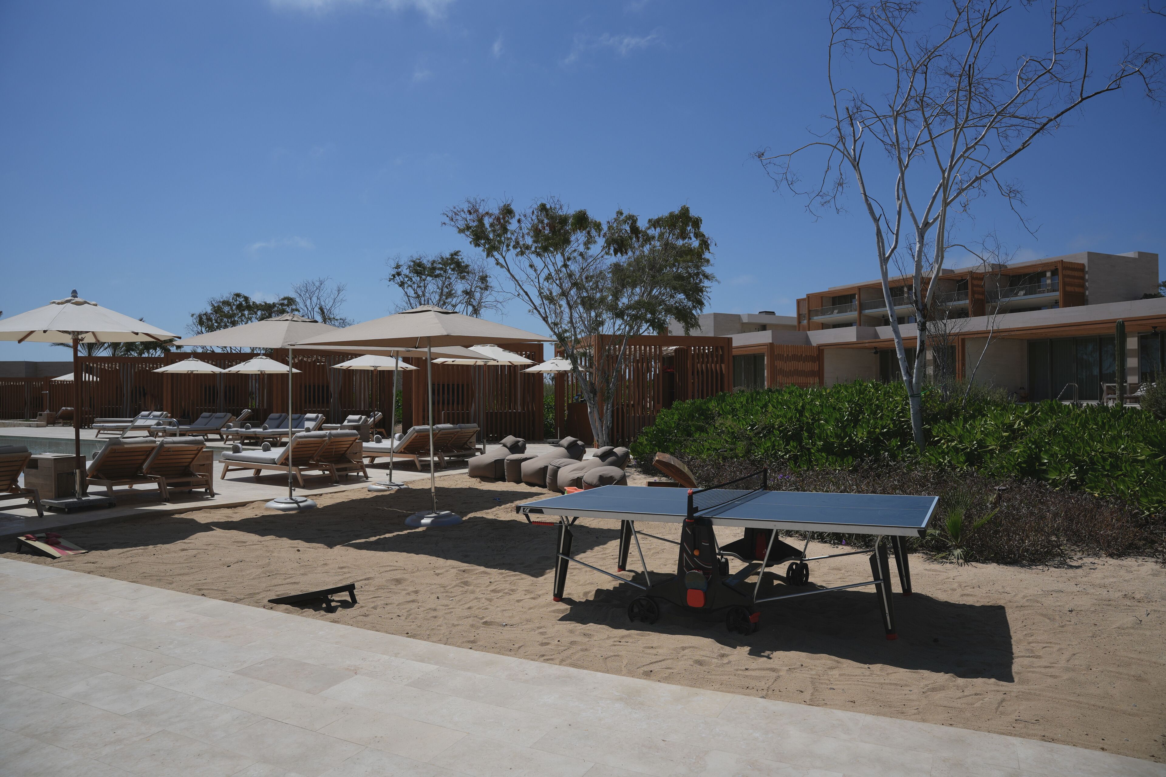 A beachside lounge area with sun loungers, umbrellas, and a ping pong table.