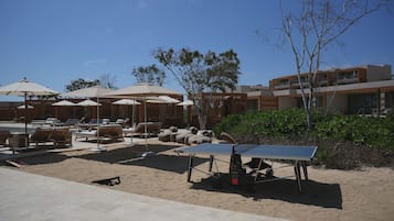 A beachside lounge area with sun loungers, umbrellas, and a ping pong table.