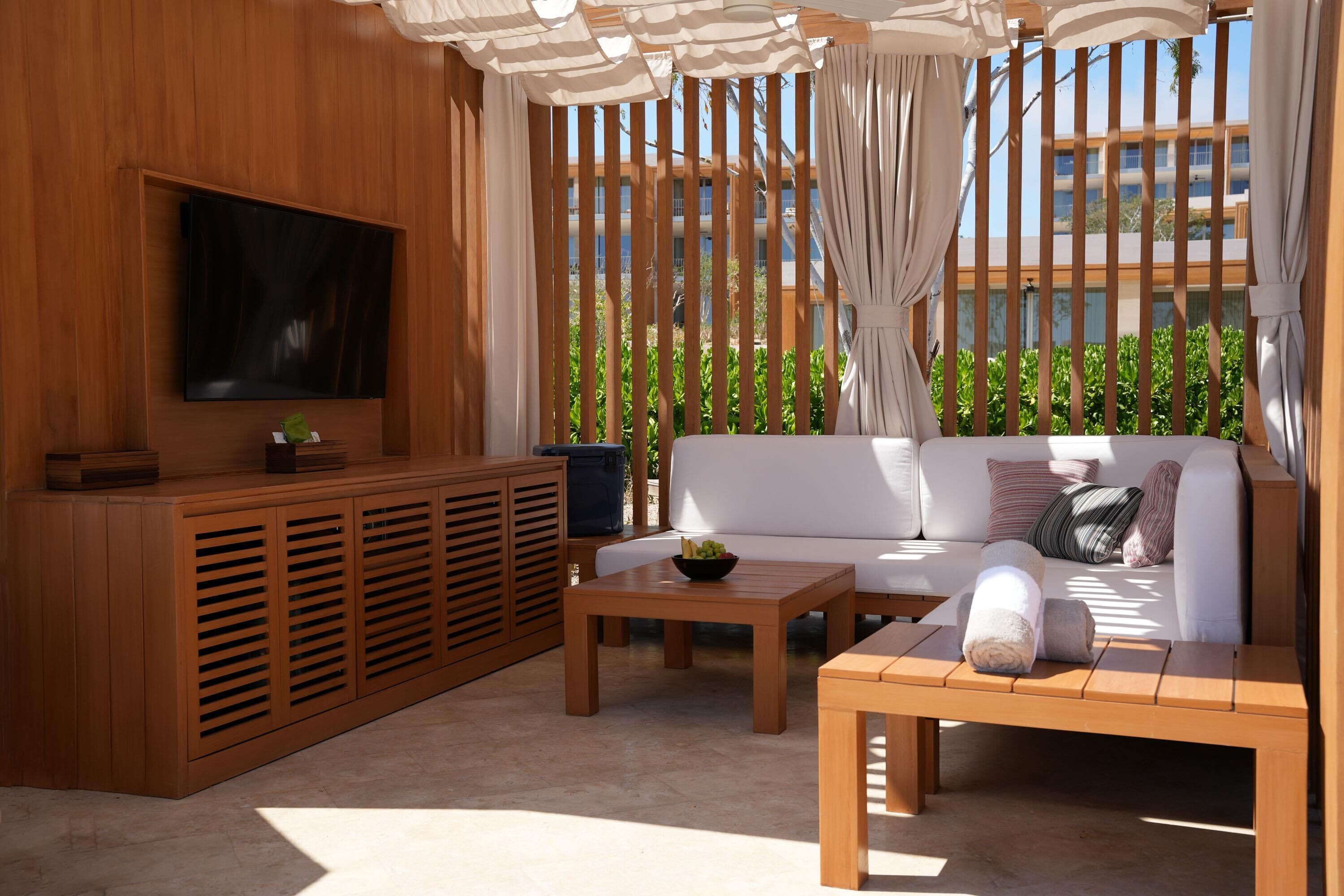 A modern outdoor living area with a sofa, a coffee table, and a TV mounted on a wooden wall.