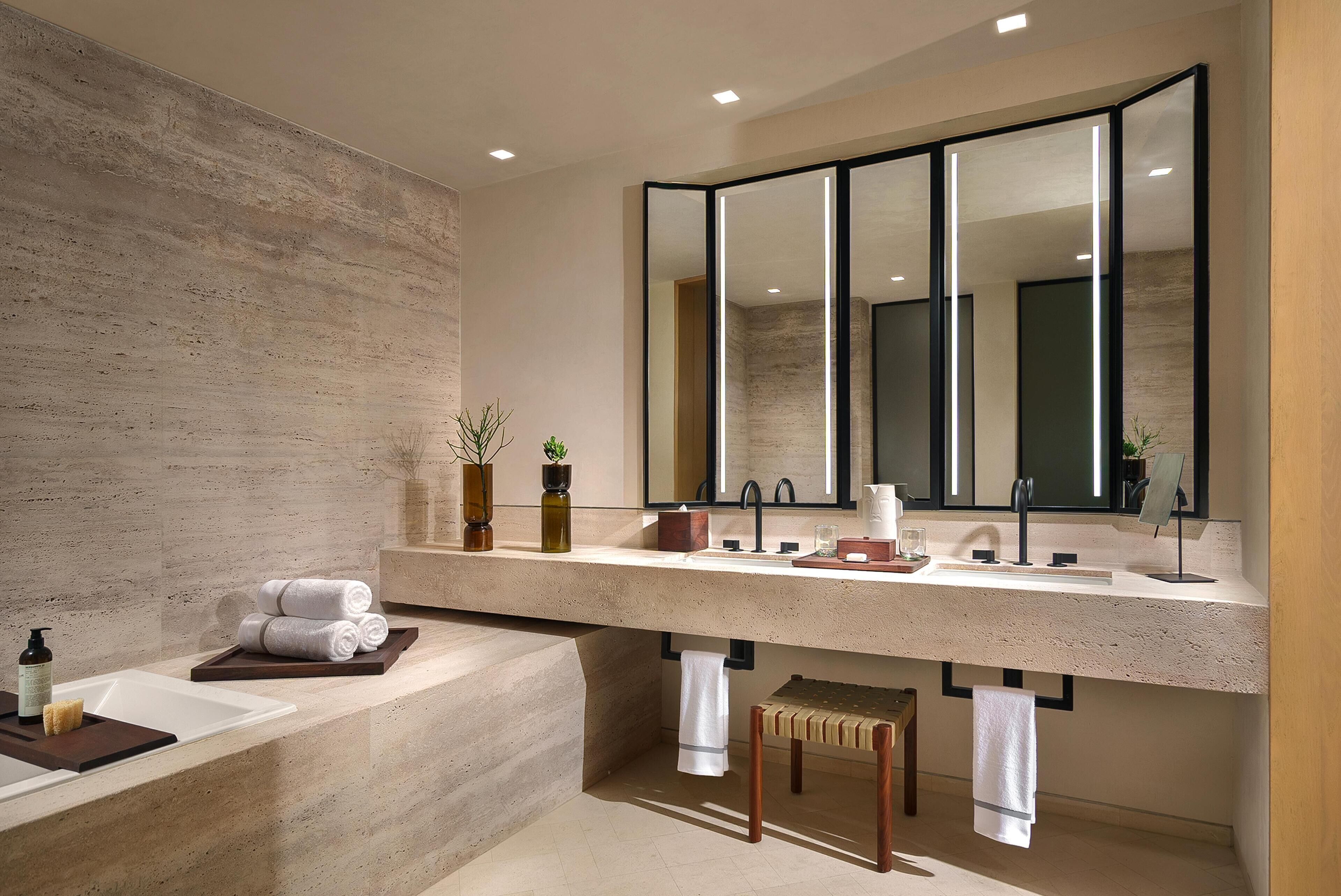 A modern bathroom with a large mirror, a bathtub, and a vanity with a sink.