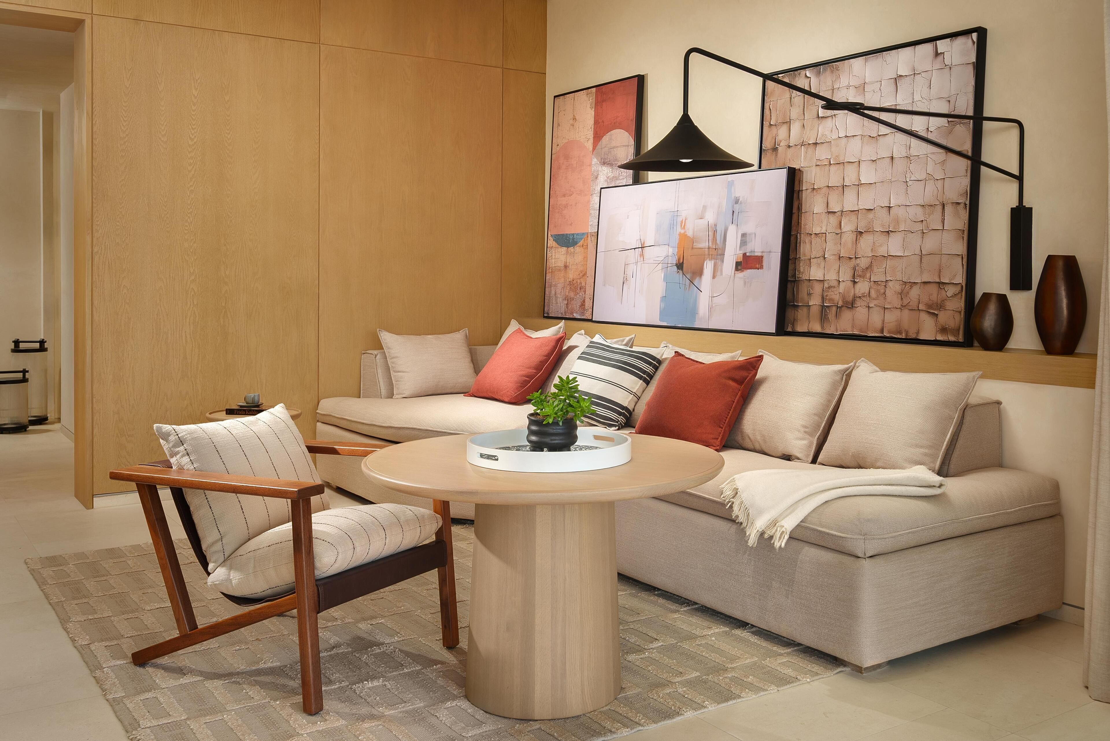Un salon moderne avec un canapé, une chaise en bois, une table basse ronde et des œuvres d’art abstraites accrochées au mur.