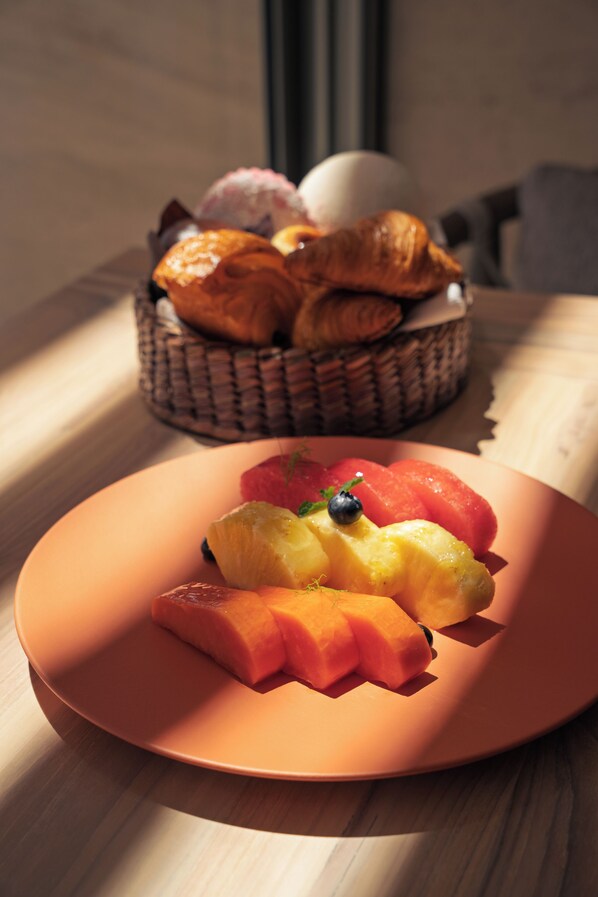 Un plato de fruta y una cesta de cruasanes sobre una mesa.